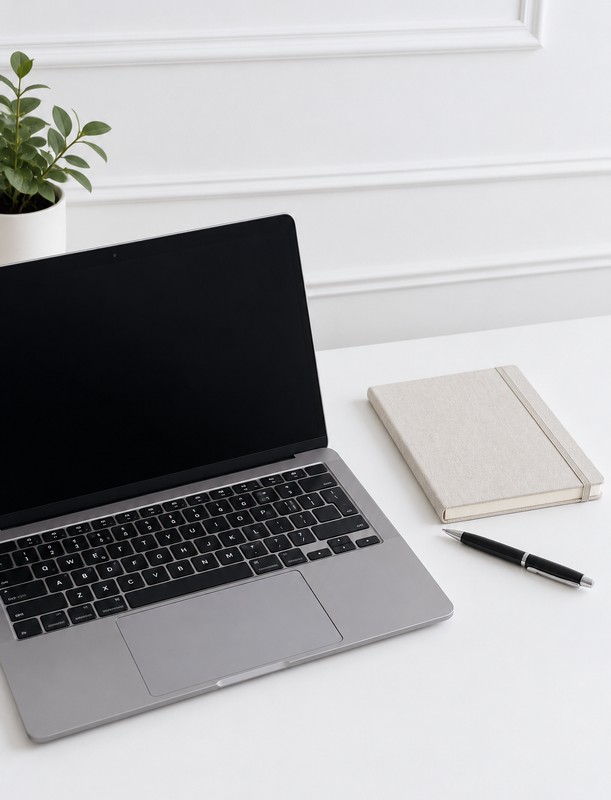 Laptop, linen notebook, and pen on a white desk